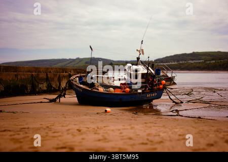 Ein Fischerboot liegt bei Ebbe an einer sandigen Küste, umgeben von einer ruhigen Küstenlandschaft. Stockfoto