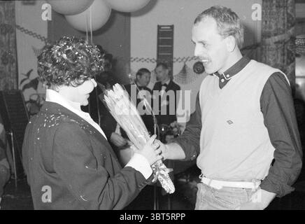 HALLE. Personal Party Color Partys, Whizgle News, Dutch Desk, Niederlande, 1950 - 2000 am 12-12-1981. Die Abbildung zeigt diese Themen. In einem lebhaften Innenbereich erfüllt ein Gefühl der Feier die Atmosphäre. Zahlreiche Ballons schweben darüber und werfen sanfte Schatten auf die Wände, die mit festlichen Dekorationen geschmückt sind. Die Farbpalette zeigt verschiedene Schattierungen, wobei der Schwerpunkt hauptsächlich auf den klassischen Schwarz-, weiß- und Grautönen liegt, wodurch sie eine zeitlose Atmosphäre erhält. Im Vordergrund stehen zwei Personen in einem warmen Austausch. Eine Person, die in einer schwarzen Jacke gekleidet ist, hält einen Blumenstrauß, dessen Farben sie andeuten Stockfoto