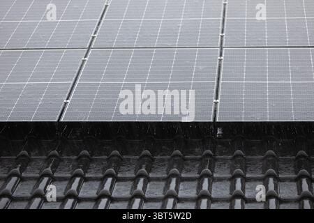 Unterkante der Solarpaneel-Anordnung auf dunklen Dachziegeln bei starkem Regen. Stockfoto