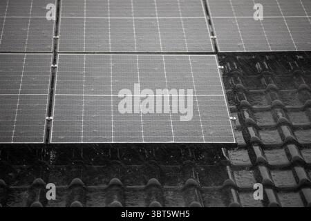 Solarpaneele und dunkle Dachziegel in landschaftlicher Ausrichtung unter starkem Regen. Stockfoto