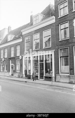 Außengebäude Jansweg Außenansicht Haarlem Jansweg The Netherlands, Whizgle News, Dutch Desk, Niederlande, 1950 - 2000 am 29-01-1968. Das Bild enthält diese Themen. Die Szene bietet einen Blick auf die Straße auf ein malerisches Stadtgebiet und zeigt eine Reihe von charmanten Gebäuden mit unterschiedlichen architektonischen Stilen. Die Strukturen sind hauptsächlich aus Ziegelsteinen gebaut und zeigen Farbvariationen von tiefrotem bis gedämpftem Braun, die ein Gefühl historischer Bedeutung widerspiegeln. Hohe, schmale Fenster zieren jede Fassade, einige mit Holzläden, die einen Blick auf die Innenräume erlauben, was eine gemütliche Atmosphäre suggeriert Stockfoto
