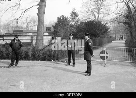Offiziere auf einer gesperrten Straße, Whizgle News, Dutch Desk, Niederlande, 1950 - 2000 am 04-1988. Diese Themen werden in der Abbildung angezeigt. Die Szene zeigt eine monochromatische Landschaft, hauptsächlich in Grautönen, die einen Hauch von Somberkeit verleiht und einen ruhigen Moment in einer urbanen Umgebung reflektiert. Im Vordergrund stehen drei in dunklen Uniformen gekleidete Figuren nahe einer Barriere, deren Haltung auf Wachsamkeit und Aufmerksamkeit für ihre Umgebung hindeutet. Links hält eine Person eine entspanntere Haltung, lehnt sich lässig an den Zaun, während die anderen beiden aufrecht stehen und leicht von der Zaunwand abgewandt sind Stockfoto