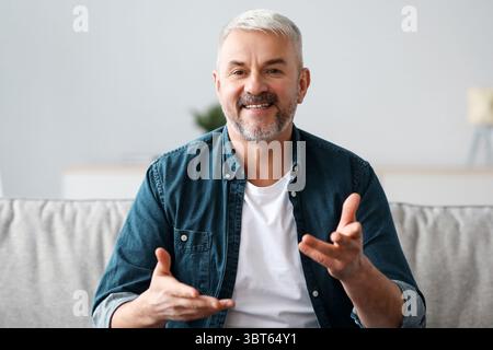 Fröhlicher, gereifter Mann, der von zu Hause aus eine Videokonferenz abhalten kann Stockfoto