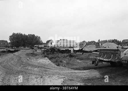 Baubeginn von Wohnungen Badhoevedorp Baustellen Häuser und Hausbau, Whizgle News, Dutch Desk, Niederlande, 1950 - 2000 am 06-10-1976. Dies sind die Themen im Bild. Die Szene zeigt eine Baustelle, die von einer riesigen Erdfläche geprägt ist, die hauptsächlich aus diffusen Grau- und Brauntönen besteht. Im Vordergrund bilden die Reifenspuren ein Zickzackmuster durch den Schmutz, das auf die Bewegung schwerer Maschinen hinweist. Unter den Maschinen dominiert ein großer Bagger in einer Ecke, dessen Arm über einem Haufen ausgehobener Erde steht, während ein weiteres Gerät Stockfoto