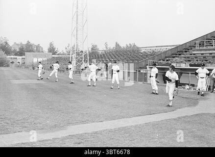 Ausbildung Niederländisch. Baseballteam Baseball Training, Whizgle News, Dutch Desk, Niederlande, 1950 - 2000 am 27-06-1972. Dies sind die Elemente im Bild. Die Szene zeigt ein Baseballtraining auf einem großen, offenen Feld. Im Vordergrund befinden sich mehrere Spieler auf dem gut gepflegten Gras, die an verschiedenen Aufwärmübungen teilnehmen. Jeder Spieler trägt eine klassische Baseball-Uniform mit einfarbigen weißen Hemden und taillierten Hosen, die einen starken Kontrast zum grünen Gras des Spielfeldes bilden. Die Personen zeigen unterschiedliche Haltungen und Bewegungen; einige Strecken sich, während andere das Werfen üben. T Stockfoto