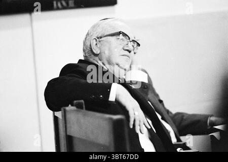 Stadtrat Van Liemt Haarlem Municipal Council, Whizgle News, Dutch Desk, Niederlande, 1950 - 2000 am 11-11-1970. Diese Themen werden in der Abbildung angezeigt. In einer bescheidenen Inneneinrichtung sitzt ein älterer Mann und zeigt ein nachdenkliches Verhalten. Er hat graue Haare und trägt eine Brille, was auf sein Alter und seine Erfahrung hindeutet. In einem dunklen Anzug gekleidet, ist seine Haltung entspannt und doch aufmerksam, wobei eine Hand elegant auf dem Arm des Holzstuhls liegt, den er besetzt. Der Hintergrund ist leicht verschwommen und zeigt andere Figuren, die auf ein Treffen oder Treffen hinweisen. Die Beleuchtung ist weich und kontrastierend und verleiht sanften SHA Stockfoto