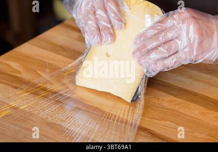 Der Ladenassistent wickelt ein Stück Käse ein Stockfoto