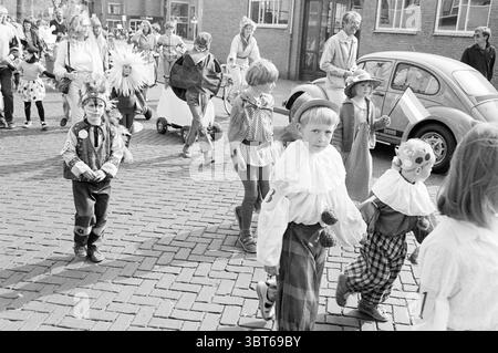 Santpoort Zuid - IJmuiden - Nieuw Vennep Queen's Day IJmuiden Niederlande, Whizgle News, Dutch Desk, Niederlande, 1950 - 2000 auf 30-04-1984. Die Abbildung zeigt diese Themen. In einer lebhaften städtischen Umgebung findet eine lebhafte Prozession statt, bei der eine Gruppe von Kindern in aufwendigen Kostümen zu sehen ist. Die Szene ist reich an verschiedenen Farbtönen, die von den hellen Farben der Kinderkleidung bis zu den gedämpften Tönen der Straße und Gebäude reichen. Die Kinder, eine Mischung aus Jungen und Mädchen, tragen eine Vielzahl von skurrilen Kleidern: Einige tragen übergroße Rüschen-Kragen, helle Clown-Outfits mit verziert Stockfoto