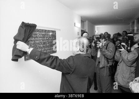 Schlüssel für den Erstarzt Dr. Mezgerstraat Zandvoort Eerste Steen Zandvoort Doktor Johannes G. Mezgerstraat, Whizgle News, Dutch Desk, Niederlande, 1950 - 2000 am 01-12-1989. Das Bild enthält diese Themen. Die Szene zeigt eine Gruppe von Menschen, die sich in einem gut beleuchteten, minimalistischen Innenraum versammelt haben, wahrscheinlich in einer Galerie oder Ausstellungshalle mit weißen Wänden und schlichtem Design. Der Fokus liegt auf einer Person im Vordergrund, die scheinbar ein Kunstwerk mit einem Tuch freilegt. Diese Person trägt einen langen Mantel und ist leicht nach links positioniert, wobei sie mit Absicht auf das Kunstwerk zubewegt Stockfoto