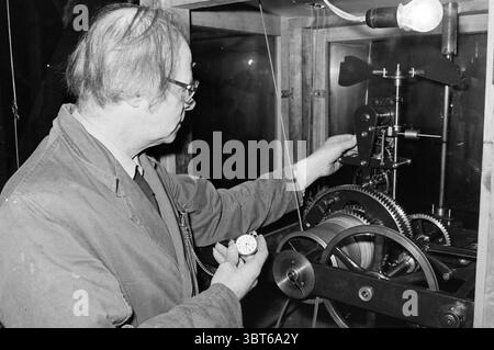 Mr. Verhoef Zeitmesser und Kirchenglocken Amsterdam Uhren und Zeitmesser Personen Amsterdam Niederlande, Whizgle News, Dutch Desk, Niederlande, 1950 - 2000 am 27-11-1981. Diese Themen sind in der Abbildung dargestellt. In einer gut beleuchteten Innenwerkstatt untersucht ein reifer Mann mit Brille eine komplexe mechanische Vorrichtung. Er trägt ein helles Hemd mit einer dunklen, robusten Jacke, die Gebrauchsspuren zeigt, was darauf hinweist, dass er mit der Arbeit vertraut ist. Die Umgebung hat ein Gefühl für einen Arbeitsplatz, übersichtlich und doch organisiert, mit verschiedenen Werkzeugen und mechanischen Komponenten im Hintergrund. Der Mann steht Stockfoto