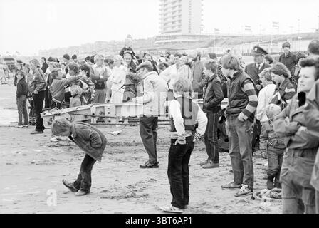 Rettungsbootdemonstration Zandvoort Demonstration Rettungsbrigade Rettungsdienst Zandvoort, Whizgle News, Dutch Desk, Niederlande, 1950 - 2000 am 05-07-1980. Diese Themen werden in der Abbildung angezeigt. Die Szene spielt an einem Sandstrand mit einer breiten Menschenmenge, die sich entlang der Küste versammelt. Die Atmosphäre ist lebhaft, aber etwas gedämpft, was auf einen bewölkten Tag hindeutet. Die Palette umfasst gedämpfte Töne – Grau- und Brauntöne dominieren den bewölkten Himmel darüber. Im Vordergrund stehen eine Vielzahl von Individuen dicht gepackt, einige blicken zum Wasser, andere scheinen mich zu verloben Stockfoto
