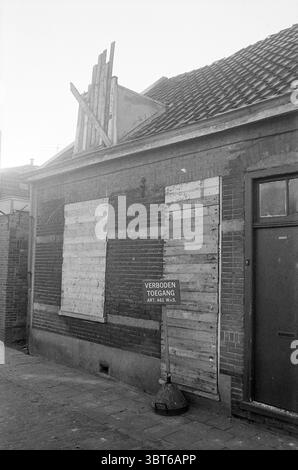 Versiegeltes Haus Beverwijk Häuser und Hausbau, Whizgle News, Dutch Desk, Niederlande, 1950 - 2000 am 15-12-1975. Das Bild enthält diese Themen. Die Szene zeigt ein verlassenes Gebäude mit einem leicht baufälligen Aussehen. Die Ziegelfassade ist überwiegend in gedämpftem Rotbraun gehalten und zeigt Gebrauchsspuren mit verblassten Farbflecken. Einige Holzdielen wurden willkürlich an den Fenstern angebracht, was den Eindruck erweckte, die Struktur zu sichern, während einige der Bretter verwittert und veraltert wirken und eine Reihe von Braun- und Grautönen aufweisen. An der Dachlinie, vertikaler Holzbalken Stockfoto