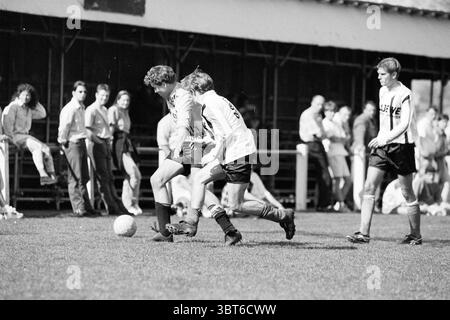 Football Schoten - HBC Velserbroek, Whizgle News, Dutch Desk, Niederlande, 1950 - 2000 am 20-04-1996. Das Bild enthält diese Themen. Die Szene zeigt einen intensiven Moment in einem Fußballspiel auf einem grasbewachsenen Feld, beleuchtet von hellem Tageslicht. Zwei Spieler, die in schwarz-weiß gestreiften Trikots gekleidet sind, sind eng mit einem Fußball zu ihren Füßen verbunden. Ein Spieler scheint den anderen auszumanövrieren, der sich heftig verteidigt. Das Gras ist ein sattes Grün mit braunen Flecken, was darauf hindeutet, dass es vom Sport abgenutzt wurde. Im Hintergrund, eine kleine Zuschauermenge c Stockfoto