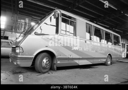 VIP-Van bei Jan de Wit, Whizgle News, Dutch Desk, Niederlande, 1950 - 2000 am 04-11-1990. Das Bild enthält diese Themen. Die Szene verfügt über einen Innenraum, der einer Garage oder Werkstatt ähnelt und sich durch eine geräumige, industrielle Atmosphäre auszeichnet. Ein großes Fahrzeug, wahrscheinlich ein Bus oder Reisebus, ist an einer Seite deutlich sichtbar positioniert. Das Äußere ist in einer gedämpften Farbpalette aus Silber und Grau lackiert und unterstreicht ein schlankes, stromlinienförmiges Profil. Die Räder des Busses sind spürbar entlüftet, was ein Gefühl der Vernachlässigung oder des Außerbetriebs des Fahrzeugs vermittelt. Sonnenlicht filtert durch die Dachfenster, casti Stockfoto