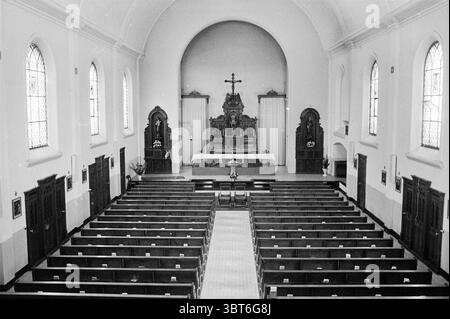 Innenraum Paterskerk IJmuiden. Innenausstattung, Whizgle News, Dutch Desk, Niederlande, 1950 - 2000 am 16-07-1971. Die Abbildung zeigt diese Themen. Die Szene zeigt einen Innenblick auf eine Kirche, die sich durch ihre hohe, bogenförmige Decke und eine geräumige, ehrfürchtige Atmosphäre auszeichnet. Reihen von Holzbänken erstrecken sich zu einem Hauptaltar am anderen Ende, wodurch ein Gefühl von Tiefe und Perspektive entsteht. Die Bänke sind ordentlich angeordnet, ihr dunkles Holz steht im Kontrast zum hellen Boden, der gut gepflegt wirkt. Natürliches Licht strömt durch mehrere große Buntglasfenster ein, was eine bunte Palette von Pattern hervorbringt Stockfoto