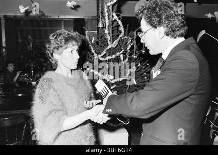 Preisverleihung goldenes Telefon HD Haarlems Dagblad etc. Und IJmuider Courant and Koeri Award Ceremony, Whizgle News, Dutch Desk, Niederlande, 1950 - 2000 am 19.12.1984. Das Bild enthält diese Themen. In einer gemütlichen, schwach beleuchteten Umgebung führen ein Mann und eine Frau ein Gespräch. Der Mann, der in einem schwarzen Anzug mit Fliege gekleidet ist, scheint ernsthaft zu sprechen und hält ein kleines Gerät, möglicherweise ein Mikrofon oder ein Aufnahmegerät, in der rechten Hand. Sein Haar ist voluminös gestylt, was zu einem edlen Look beiträgt. Die Frau steht ihm gegenüber und trägt einen weichen, strukturierten Pullover Stockfoto
