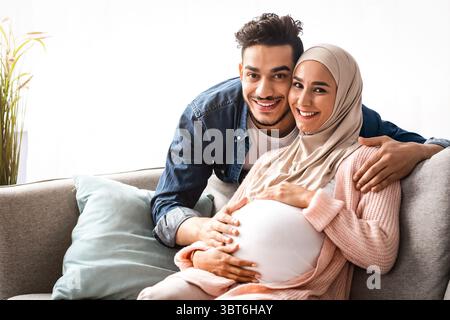 Schwangere muslimische Paar umarmt zu Hause, sitzen auf der Couch im Wohnzimmer Stockfoto