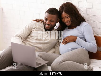 Glückliches schwangeres Paar, das Möbel für das Babyzimmer online auswählt Stockfoto