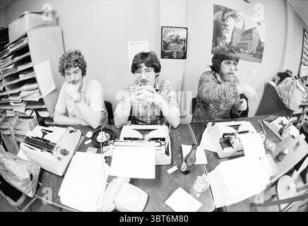 Making Sinterklaas Poems Haarlems Dagblad St. Nicholas Sinterklaas, Whizgle News, Dutch Desk, Niederlande, 1950 - 2000 am 24-11-1978. Das Bild enthält diese Themen. Die Szene zeigt drei Personen, die an einem Holztisch sitzen und sich jeweils auf ihre eigene Schreibmaschine konzentrieren. Der Tisch ist überfüllt mit verstreuten Papierbögen und ein paar Gegenständen, darunter ein Telefon und eine Flasche. Die erste Person links hat lockiges braunes Haar und trägt ein helles Hemd. Er wirkt besinnlich, mit den Händen, die sich in der Nähe seines Mundes befinden. In der Mitte hat die zweite Person dunkles, welliges Haar und Sport-gla Stockfoto