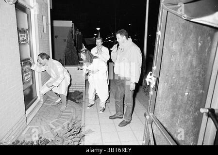 Velserbroek 50 Jahre alt in der Nacht + Orgel Velserbroek, Whizgle News, Dutch Desk, Niederlande, 1950 - 2000 am 26-03-1991. Diese Themen sind in der Abbildung dargestellt. Die Szene spielt in einer schwach beleuchteten Straße bei Nacht, wo eine Gruppe von vier Personen in einem faszinierenden Moment festgehalten wird. Im Vordergrund steht ein Mann in einem weißen Laborkittel, der sich nach unten hockt und durch ein Glasfenster blickt, als ob er etwas im Inneren untersuchen würde. Seine Haltung deutet auf Neugier und Dringlichkeit hin. Neben ihm steht eine Frau mit wilden, lockigen Haaren leicht gewendet, in einem ähnlichen Laborkittel gekleidet und scheint in Gesprächen zu sein Stockfoto