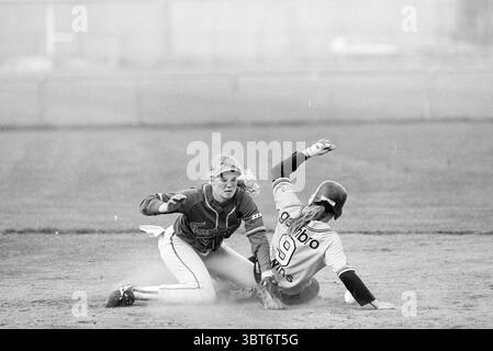Softball Terrasvogels - Twins, Whizgle News, Dutch Desk, Niederlande, 1950 - 2000 am 11-07-1997. Dies sind die Elemente im Bild. In einer dynamischen Outdoor-Szene werden zwei Athleten mitten in einem Wettkampfmoment auf einem Baseballfeld festgehalten. Die Umgebung weist eine Weite aus Schmutz und Gras auf, was auf ein aktives Spiel hinweist. Ein Spieler trägt eine dunkle Uniform mit mehrschichtigen Texturen, hockt sich tief bis zum Boden, ihr Gesichtsausdruck konzentriert und intensiv, was die Entschlossenheit unterstreicht. Sie hat lange Haare, die nach hinten gezogen werden, was ihren konzentrierten Blick betont, während sie sich darauf vorbereitet, den gegnerischen Spieler zu markieren Stockfoto
