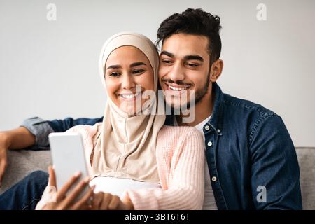 Fröhliche Schwangeren Im Nahen Osten Ehegatten Surfen Im Internet Auf Dem Smartphone Zusammen Zu Hause Stockfoto