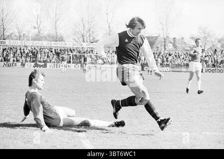 Haarlem - Excelsior Football Haarlem, Whizgle News, Dutch Desk, Niederlande, 1950 - 2000 am 04-05-1975. Diese Themen sind in der Abbildung dargestellt. Die Szene fängt einen Moment auf einem belebten Fußballfeld voller Energie und Bewegung ein. Das Gras ist lebendig und gepflegt, im Kontrast zum leuchtend blauen Himmel darüber, der auf klares Wetter hinweist. Im Vordergrund wird ein Spieler in einer dunklen Uniform mit Streifenmuster in einer Farbkombination gefangen, die ein Gefühl von Kraft und Konzentration vermittelt. Sein Ausdruck ist intensiv, während er an einem anderen Spieler vorbeimanövriert, der auf der Gr ist Stockfoto