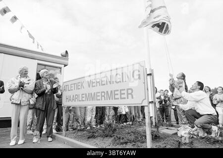 Enthüllung des Namensschildes des des Athlemmermeer-Vereins Haarlemmermeer, Whizgle News, Dutch Desk, Niederlande, 1950 - 2000 im Jahr 1990. Das Bild enthält diese Themen. In der Szene versammelt sich eine Gruppe von Menschen im Freien und schafft eine lebhafte Atmosphäre, die mit einem Gefühl der Feier und Gemeinschaft erfüllt ist. Im Vordergrund stehen mehrere Personen, darunter ein älteres Ehepaar und ein Mann, der neben einem Fahnenmast kniet und an der zeremoniellen Handlung des Flaggenhissens beteiligt ist. Der Mann, in lässiger Kleidung gekleidet, scheint konzentriert und entschlossen zu sein, während er das Seil sorgfältig verwaltet. Die älteren Menschen, wahrscheinlich in ihren siebi Stockfoto