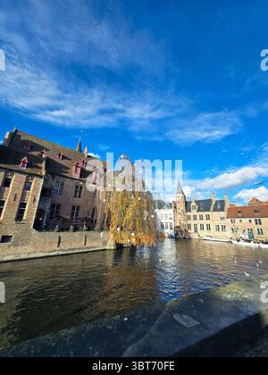 Friedliche Kanalszene in Brügge, Belgien, eingerahmt von Herbstbäumen und historischen Gebäuden unter einem dramatischen blauen Himmel. Stockfoto