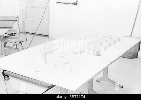 Rudolf Steiner School First Pile Scale Modell 01-03-1965, Whizgle News, Dutch Desk, Niederlande, 1950 - 2000 am 02-03-1965. Das Bild enthält diese Themen. Die Szene zeigt einen Arbeitsbereich, der sich um eine große, Ebene Fläche dreht, auf der ein detailliertes Architekturmodell erstellt wird. Das Modell, das aus Materialien wie Holz und Papier gefertigt ist, zeigt eine Reihe von Gebäuden, die in geordneter Weise angeordnet sind. Die Strukturen haben einen minimalistischen Stil, mit klaren Linien und scharfen Winkeln, die eine moderne Ästhetik zeigen. Die Umgebung zeichnet sich durch eine helle, gut beleuchtete Umgebung mit weicher, diffuser Li aus Stockfoto