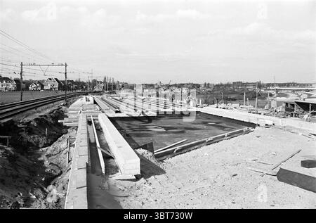 Bau des nördlichen Teils des westlichen Randweges zwischen Bahn und Kleverlaan. Bau von Hochgleis und Viadukten über die neue Straße Haarlem Westelijke Randweg Nederland., Whizgle News, Dutch Desk, Niederlande, 1950 - 2000. Diese Themen werden in der Abbildung angezeigt. Die Szene zeigt eine weitläufige Baustelle, die sich über den Vordergrund erstreckt und eine riesige Fläche mit Roherde und Baumaterialien zeigt. Große, unfertige Betonplatten sind in ordentlichen Reihen angeordnet, was auf den Rahmen einer noch zu vollendenden Struktur hindeutet. Die Textur des Betons wirkt rau, Co Stockfoto