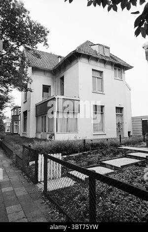 Bericht Jugendzentrum Zandvoort Report, Whizgle News, Dutch Desk, Niederlande, 1950 - 2000 am 23-08-1971. Diese Themen werden in der Abbildung angezeigt. Die Szene zeigt ein großes, zweistöckiges Haus, das sich durch seine traditionelle Architektur auszeichnet. Das Äußere ist größtenteils weiß, mit dunklen Akzenten um die Fenster und das Dach. Das Dach ist geneigt und verfügt über einen deutlichen Giebelgiebel, der den Charme des Hauses noch verstärkt. Im Vordergrund führt ein Weg aus quadratischen Steinen zum Eingang hinauf, der von einem niedrigen Zaun aus Holzdielen begrenzt wird, der dunkel bemalt ist. Der Zaun umschließt ein Stück ungepflegtes Gras, was darauf hindeutet, dass ein l Stockfoto