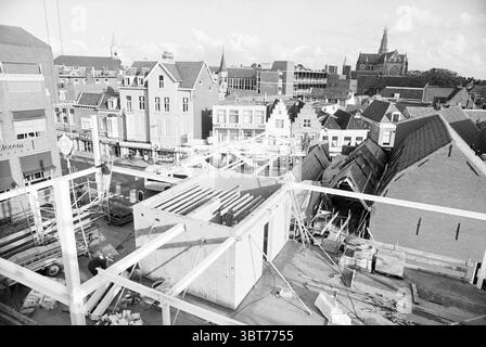 Construction Work Raaks, Whizgle News, Dutch Desk, Niederlande, 1950 - 2000 am 23-10-1994. Diese Themen werden in der Abbildung angezeigt. Die Szene zeigt eine geschäftige urbane Umgebung aus erhöhter Position. Im Vordergrund befindet sich eine Baustelle, die von einer Betonkonstruktion mit Gerüsten und Holzbalken dominiert wird, was auf eine laufende Entwicklung hinweist. Die scharfen Linien der Konstruktion stehen in starkem Kontrast zu den kunstvolleren architektonischen Elementen der umliegenden Gebäude. Auf der linken Seite befindet sich eine Reihe traditioneller Häuser im niederländischen Stil mit Giebeldächern, die in gedämpften Beige- und Hellfarben gestrichen sind Stockfoto