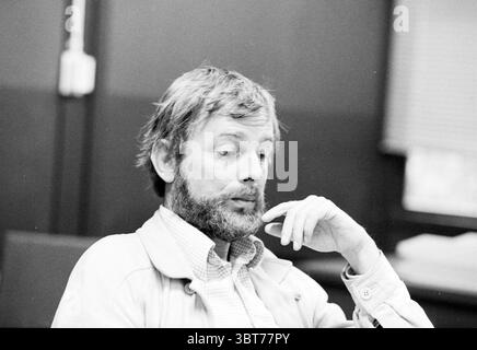 Porträt von HR Heus Rektor Haarlemmermeerlyceum Portraits, Whizgle News, Dutch Desk, Niederlande, 1950 - 2000 am 26-09-1979. Diese Themen sind in der Abbildung dargestellt. In der Szene sitzt ein Mann mit einem nachdenklichen Ausdruck, der sich leicht nach vorne beugt. Sein Haar ist zerzaust und etwas ungepflegt, mit Grau- und Hellbraun-Tönen. Ein Vollbart umrahmt sein Gesicht und verleiht ihm ein Gefühl der Reife. Er scheint in der Besinnung verloren zu sein, sein Blick nach unten gerichtet, während er sein Kinn auf einer Hand auflegt und die Finger seine Lippen in einer nachdenklichen Geste berühren. Die Einstellung enthält gedämpfte, stummgeschaltete Farben, die von dominiert werden Stockfoto