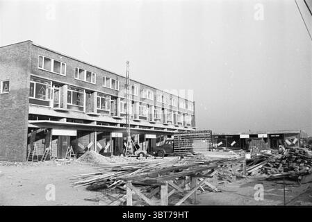 Neuer Komplex Schalkwijk Häuser und Gebäude, Whizgle News, Dutch Desk, Niederlande, 1950 - 2000 am 26-01-1961. Diese Themen sind in der Abbildung dargestellt. Die Szene zeigt eine Baustelle mit Schwerpunkt auf einer Reihe neu errichteter Gebäude. Die Architektur verfügt über mehrere Ebenen, von denen jede mit Reihen von Fenstern verziert ist, die nicht verziert sind und funktionell wirken, was ein zeitgenössisches Design andeutet. Das Äußere des Gebäudes zeichnet sich vor allem durch einen gedämpften Ziegelton aus, der durch die leicht reflektierenden Glasscheiben ergänzt wird. Im Vordergrund sind verschiedene Baumaterialien verstreut Stockfoto