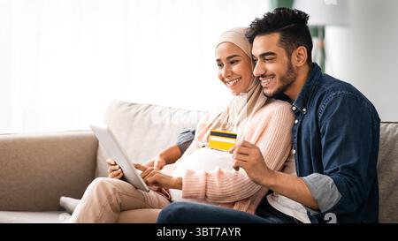 Fröhliche schwangeren muslim paar online einkaufen, mit Kreditkarte und digitalen Tablet Stockfoto