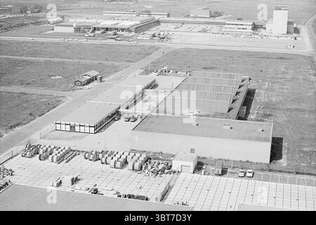 Erw. Tree Ruigrok Exterior, Whizgle News, Dutch Desk, Niederlande, 1950 - 2000 am 01-09-1972. Die Abbildung zeigt diese Themen. Die Szene präsentiert eine weitläufige, von oben aus betrachtete Industrielandschaft. Ein großes, rechteckiges Gebäude nimmt den Vordergrund ein, dessen flaches Dach von mehreren Lüftungsöffnungen oder Kanälen unterbrochen wird. Diese Struktur wird von einem sorgfältig angeordneten, mit Beton gepflasterten Bereich begrenzt, in dem zylindrische Objekte, möglicherweise Tanks oder große Container, ordentlich angeordnet sind und ein organisiertes Erscheinungsbild zeigen. Darüber hinaus gibt es weitläufige Gebäude, die sich über den Hintergrund erstrecken. Einige davon Stockfoto