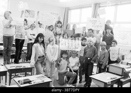 Schüleraktion „Master Must Stay“, Whizgle News, Dutch Desk, Niederlande, 1950 - 2000 am 24-05-1983. Das Bild enthält diese Themen. In einem hellen, geräumigen Klassenzimmer steht eine Gruppe von Kindern im Vordergrund und füllt den Raum mit Energie und Zweck. Die Wände sind mit farbenfrohen pädagogischen Plakaten geschmückt, die der Szene eine lebendige Kulisse verleihen. Die Kinder unterscheiden sich in Alter und Größe, mit einer vielfältigen Mischung aus Frisuren und Kleidungsstilen, die ein lässiges Erscheinungsbild am Schultag widerspiegeln. Einige Schüler tragen Pullover und T-Shirts, während andere Jeans und Turnschuhe tragen. Ein Sinn Stockfoto