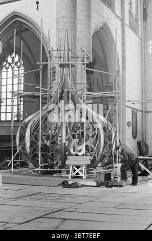 Arbeiten an der Zwiebelarbeit der Grote oder Sint-Bavokerk Klopfen der Spinnakel mit Blei Grote Kerk Haarlem Kirchen St. Bavokerk Arbeit Haarlem Grote Markt the Netherlands, Whizgle News, Dutch Desk, Niederlande, 1950 - 2000 am 02-02-1965. Dies sind die Themen im Bild. Die Szene ist in einem geräumigen Innenraum angesiedelt, wahrscheinlich in einer Kirche oder Kathedrale, die von ihrer großen Architektur geprägt ist. Hoch aufragende Steinwände mit großen Buntglasfenstern, die die Umgebung mit gedämpftem Licht durchleuchten und weiche, farbenfrohe Muster auf dem Boden hinterlassen. Im Vordergrund befindet sich ein großer Kronleuchter unter der Konstruktion Stockfoto