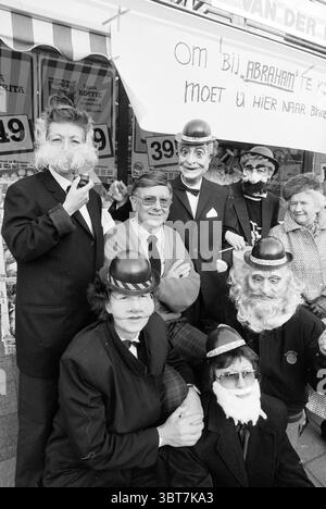 Herr Van Hulst 50 Jahre Geburtstage Heemstede Niederlande, Whizgle News, Dutch Desk, Niederlande, 1950 - 2000 am 27.01.1989. Diese Themen sind in der Abbildung dargestellt. Die Szene zeigt eine Gruppe von Einzelpersonen, die in aufwendigen Kostümen gekleidet sind und jeweils eigene Gesichtsmasken tragen, die bärtigen Männern mit dicken Schnurrbärten ähneln. Die Kleidung ist formell, mehrere Personen tragen Anzüge und Hüte und tragen so zu einer verspielten und doch raffinierten Atmosphäre bei. Die Umgebung scheint ein Außenbereich zu sein, möglicherweise in der Nähe eines Marktes oder eines Geschäfts, wie der Hintergrund mit Hinweisen auf kommerzielle Schilder A andeutet Stockfoto