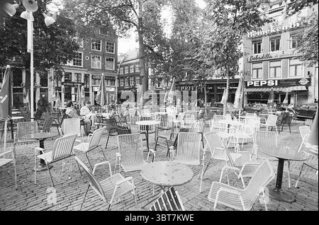 Terrassen auf dem Leidseplein mit dem Leidseplein Theater an der Ecke Amsterdam Leidseplein Niederlande, Whizgle News, Dutch Desk, Niederlande, 1950 - 2000 am 07-08-1973. Das Bild enthält diese Themen. Die Szene zeigt einen belebten Platz im Freien, der von einer Reihe leerer Metallstühle und Tische geprägt ist, die in ordentlichen Reihen auf einer gepflasterten Fläche angeordnet sind. Die Stühle, die sich durch ihre weiß-blau gestreiften Muster auszeichnen, erwecken ein Gefühl von ungezwungenem Essen, während die kleinen, runden Tische überall verteilt sind und Gäste zum Entspannen und Genießen der Atmosphäre einladen. Hohe Bäume mit üppigen, grünen Fol Stockfoto