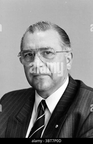 DRS. STAU. Von. Tienen VNU, Whizgle News, Dutch Desk, Niederlande, 1950 - 2000 am 24-03-1992. Diese Themen werden in der Abbildung angezeigt. Die Szene zeigt einen Mann mit nachdenklichem Ausdruck, der in einem maßgeschneiderten Anzug mit Nadelstreifenmuster gekleidet ist. Sein Haar ist zurückgeschliffen und zeigt graue Fäden und ein ordentliches Aussehen. Er trägt eine große, runde Brille, die seinem Verhalten eine akademische Atmosphäre verleiht. Der Anzug wird durch eine Krawatte mit diagonalen Streifen ergänzt, die einen dezenten Kontrast zu seiner Gesamtkleidung bildet. Der Hintergrund ist ein sanfter Gradienten, der zu einem professionellen und seriösen AT beiträgt Stockfoto