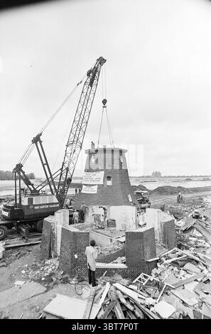 Mills, Whizgle News, Dutch Desk, Niederlande, 1950 - 2000 am 01-08-1974. Dies sind die Elemente im Bild. Die Szene zeigt eine Baumaßnahme, die sich um ein historisches Gebäude, wahrscheinlich eine Windmühle, in einem etwas industriellen Umfeld dreht. Die Windmühle mit einer ausgeprägten, sich verjüngenden Turmform wurde teilweise rekonstruiert und zeigt freiliegende Mauerwerke und Überreste ihrer früheren Form. Um diesen Schwerpunkt herum befindet sich eine Landschaft, die von Trümmern geprägt ist, darunter verstreute Holzdielen und Baumaterialien, die dem Gebiet ein ungepflegtes, t Stockfoto