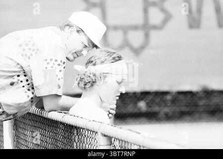 Tennis J. Knijn, Whizgle News, Dutch Desk, Niederlande, 1950 - 2000 am 06-06-1995. Diese Themen sind in der Abbildung dargestellt. Die Szene zeigt zwei Personen, die in einem Moment der Interaktion aktiv sind, gekennzeichnet durch eine etwas lässige, aber aufmerksame Dynamik. Im Vordergrund lehnt sich ein junger Mann an einen Maschendrahtzaun, mit leicht geneigtem Kopf, was auf Nachdenken oder einen Moment tiefen Denkens hindeutet. Er hat lockige Haare und trägt ein Bandana, das sich um seine Stirn schmiegt und auf eine entspannte oder sportliche Atmosphäre hindeutet. Seine Kleidung ist schlicht, aber mit einem hellen Hemd ist er lässig. Etwas zurück Stockfoto