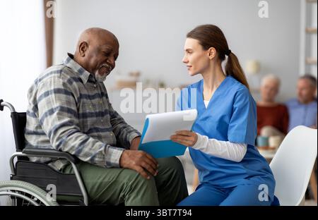 Hübsche Frau in Arbeitskleidung, die schwarzen älteren Mann beim Ausfüllen von Papieren hilft Stockfoto