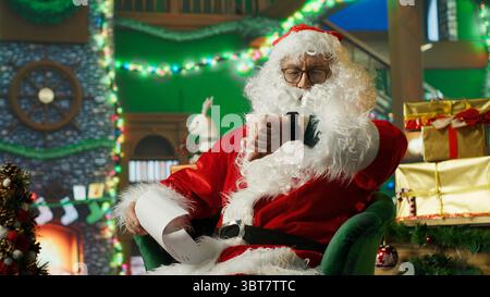 Die Person im Weihnachtskostüm wurde alarmiert, nachdem sie eindöst und spät dran war, Geschenke an Kinder zu liefern. Der Weihnachtsmann wacht auf, nachdem er auf dem Sessel eingeschlafen ist, während er Briefe von Kindern liest, Kamera A Stockfoto