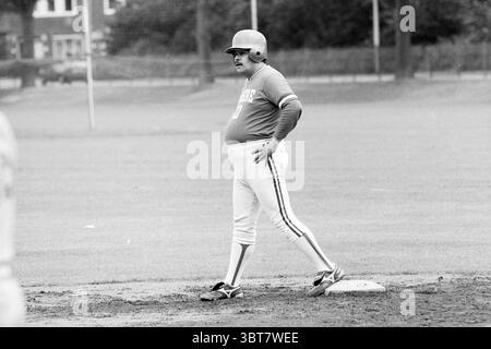 Softball Männer: Bloemendaal-Almere Bloemendaal, Whizgle News, Dutch Desk, Niederlande, 1950 - 2000 am 22-06-1991. Diese Themen sind in der Abbildung dargestellt. Die Szene zeigt einen Baseballdiamanten unter einem bewölkten Himmel, was auf einen bewölkten Tag hindeutet. Das Gras, das das Feld umgibt, ist ein leuchtendes Grün, sorgfältig gepflegt und dennoch weich unter den Füßen. Im Vordergrund steht ein Spieler selbstbewusst auf einer Basis. Er trägt ein tailliertes, kurzärmeliges Trikot, dazu eine helle Hose mit einem einzelnen Streifen an der Seite. Das Trikot ist in einem tiefen Farbton gehalten, der sich stark von seiner Kleidung abhebt. Seine Rundung Stockfoto