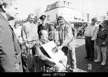 Inbetriebnahme des Strommarktes Florisstraat Inbetriebnahme Haarlem Floresstraat, Whizgle News, Dutch Desk, Niederlande, 1950 - 2000 am 30-03-1989. Das Bild enthält diese Themen. Die Szene fängt die lebhafte Atmosphäre des Freiluftmarktes ein. Eine Gruppe von Menschen versammelt sich in einem Halbkreis um einen Mann im Rollstuhl, der im Mittelpunkt der Aufmerksamkeit zu stehen scheint. Er trägt legere Kleidung, trägt eine Brille und scheint sich in ein freundliches Gespräch zu verwickeln. Sein Ausdruck deutet auf Unterhaltung hin, vielleicht genießt er die Aufmerksamkeit. Um ihn herum sind mehrere Individu Stockfoto