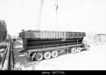 Neubau Zuckerfabrik Halfweg C.M.S. Halfway, Whizgle News, Dutch Desk, Niederlande, 1950 - 2000 am 05-09-1978. Das Bild enthält diese Themen. Die Szene zeigt einen großen Flurförderzeug, der auf einer Baustelle geparkt ist. Das Chassis des Lkw ist robust und metallisch und verfügt über mehrere Räder, die ein Gefühl von Gewicht und Festigkeit vermitteln. Es verfügt über ein Flachbett, das sich horizontal ausdehnt und einen großen, dunklen Behälter mit einem scharfen, eckigen Design zeigt. Der Behälter ist mit einer mattschwarzen Oberfläche lackiert und hebt sich von den helleren Tönen der Umgebung ab. Im Hintergrund Stockfoto