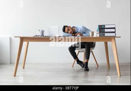 Erschöpfter Junger Mann Schläft Bei Der Arbeit Und Sitzt Am Schreibtisch Stockfoto
